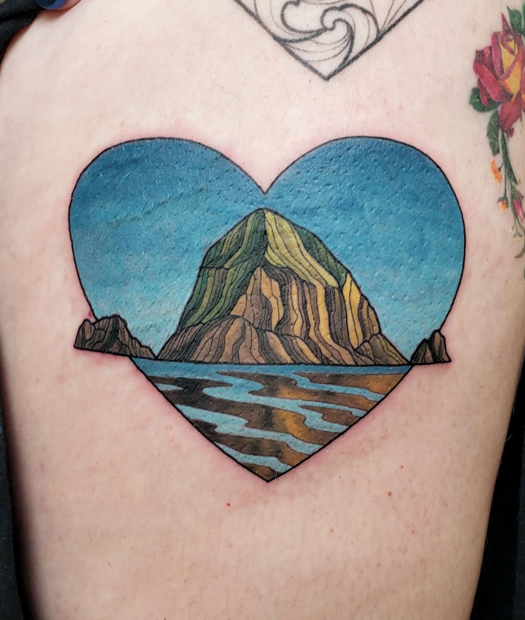Colorful tattoo of a mountain landscape inside a heart shape on a person's chest.
