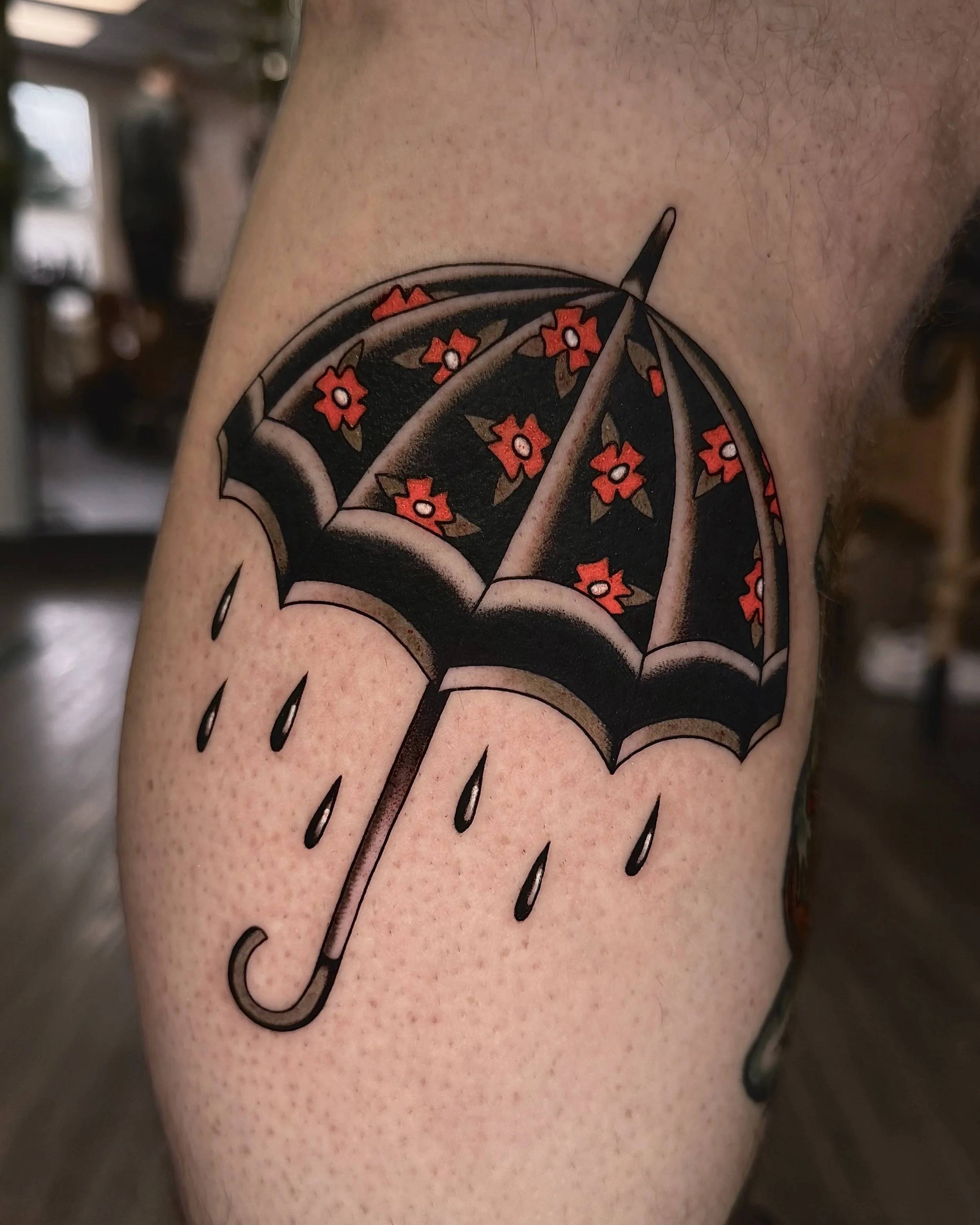 A tattoo of a black umbrella with small red flowers and raindrops on the person's upper arm.