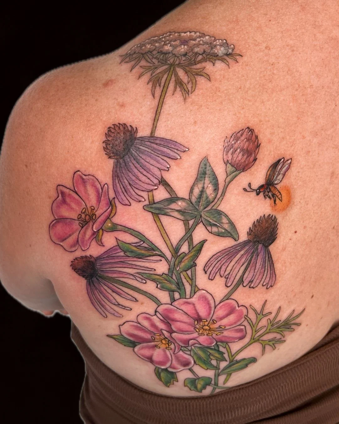Colorful floral tattoo with pink, purple, and brown flowers, green leaves, and a bee on the right side.