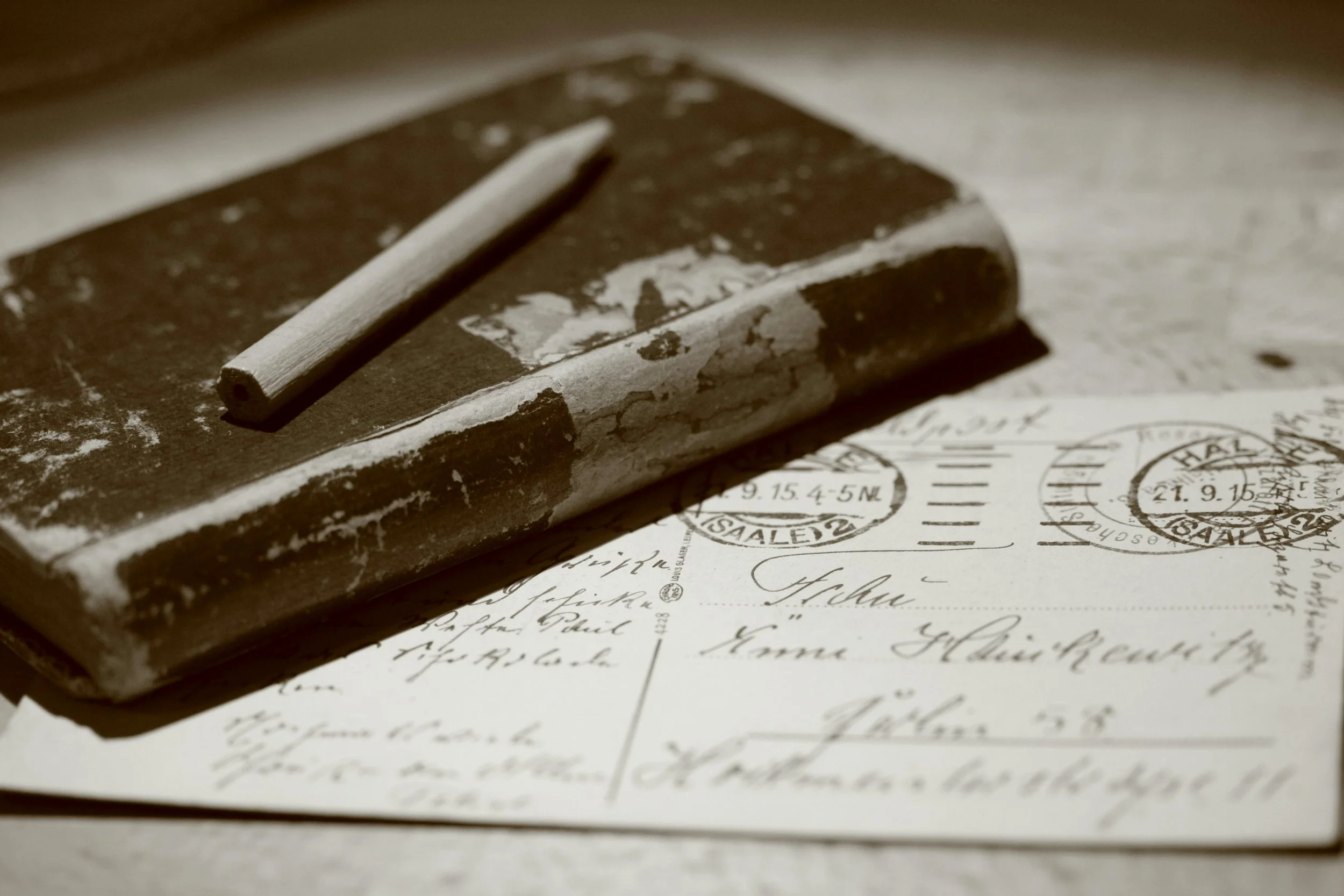 A vintage brown book with a white chalk or crayon on top, resting on handwritten handwritten letters or documents.