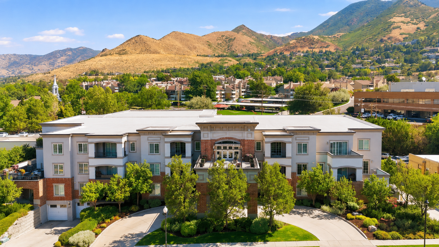 Aerial view of a modern apartment complex with trees, mountains, and a clear blue sky in the background.
