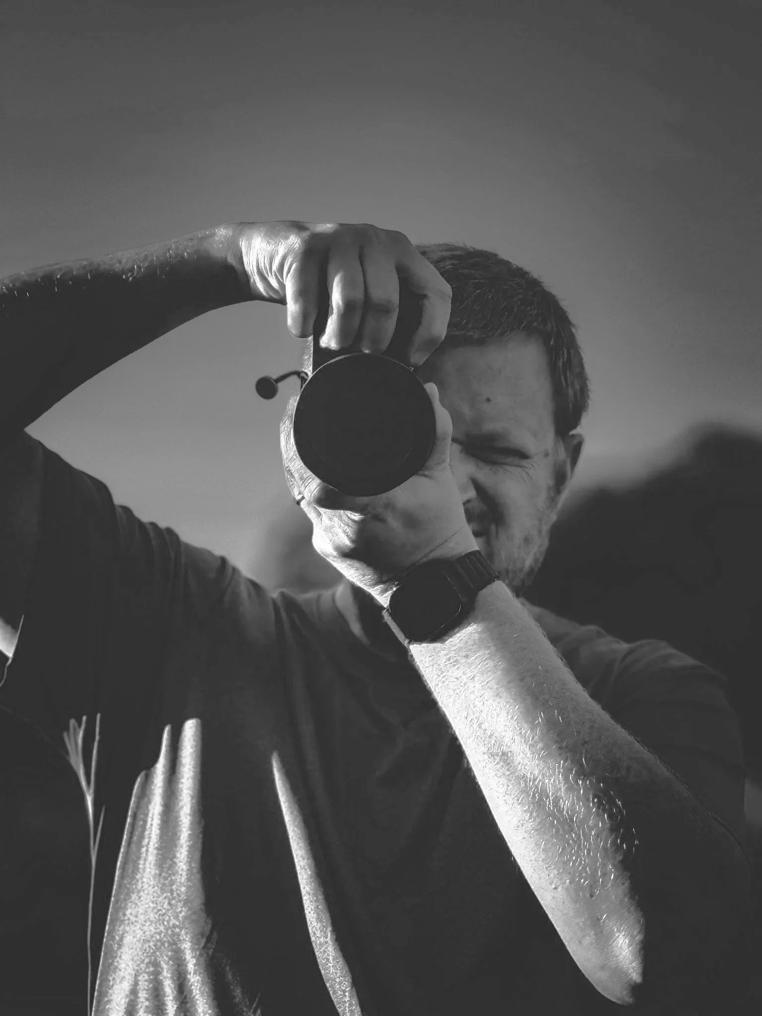 Justin DeCastra raising a camera to his eye, in a black and white portrait.