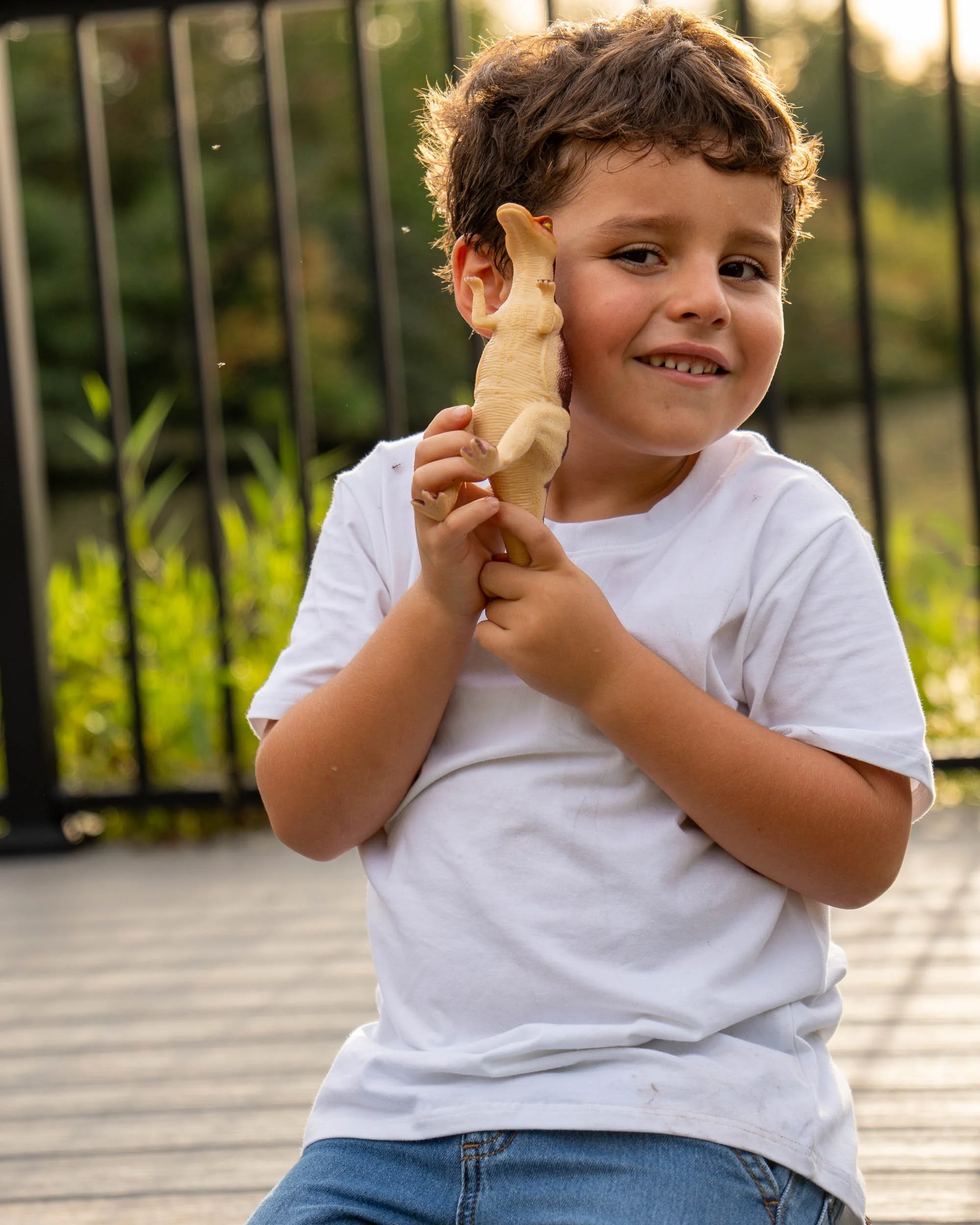 A smiling boy holds a toy dinosaur up to his cheek.