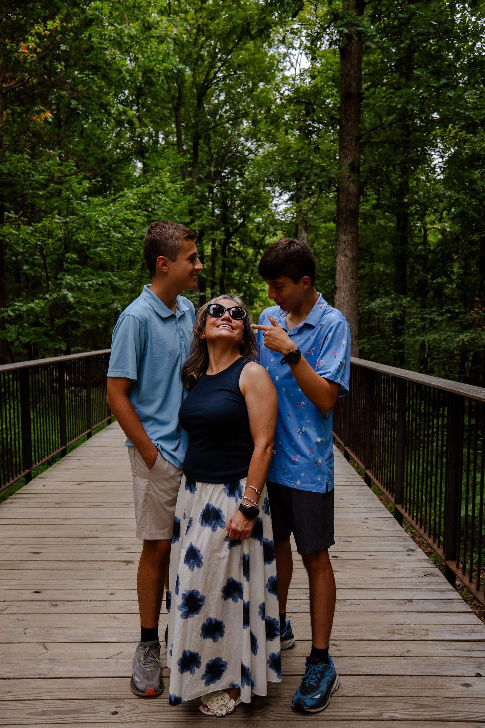 Four people, three men and one woman, are standing on a wooden bridge surrounded by trees. They are smiling and enjoying each other's company.