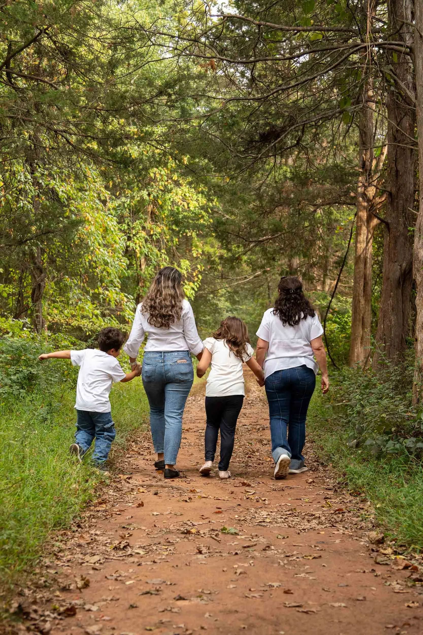 Family of four walking away down a shaded dirt trail, the little boy running ahead with his arms out.