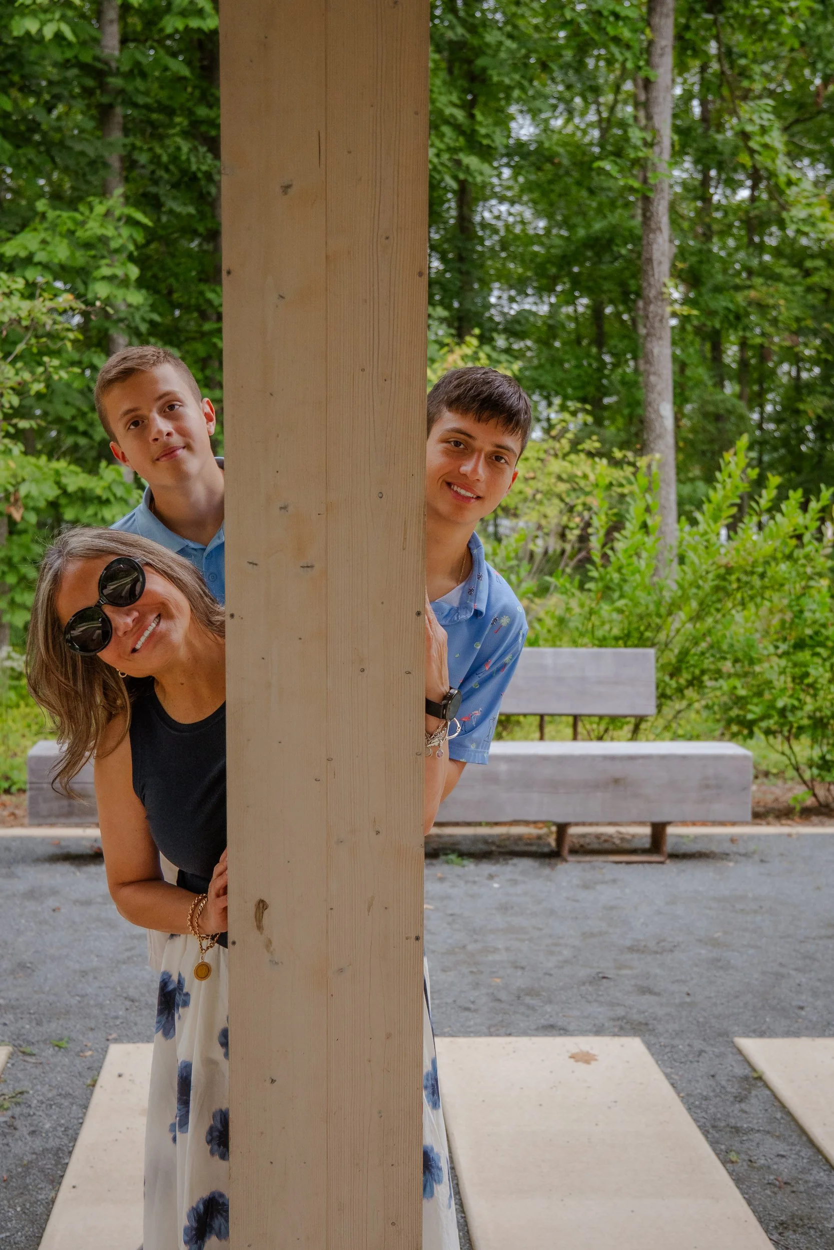 Mother and her two teenage sons peeking out from behind a wooden post at a park pavilion.