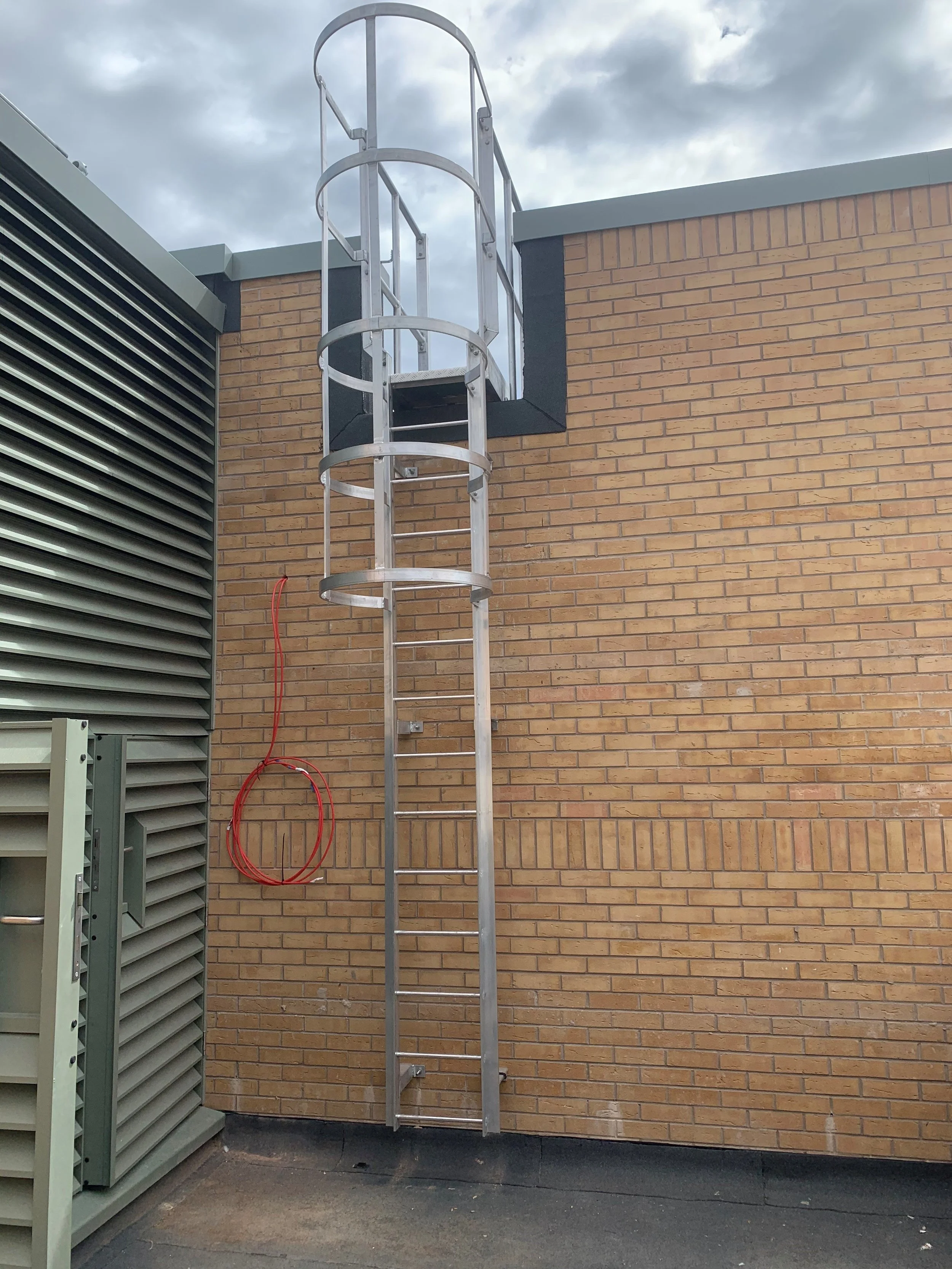 Stainless steel roof access ladder with safety cage and parapet crossover