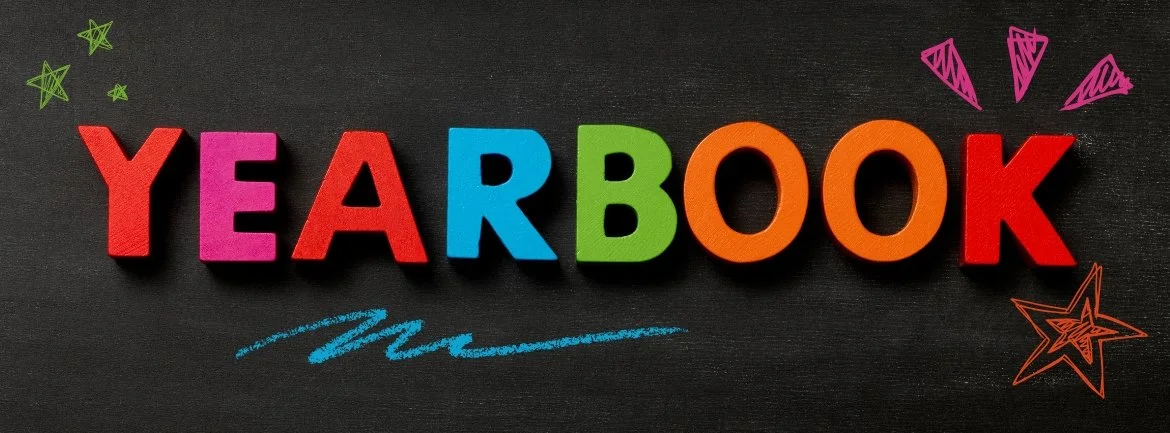 Colorful wooden letters spelling 'YEARBOOK' arranged on a black chalkboard background, decorated with doodles of stars and triangles in pink, green, orange, red, purple, and blue