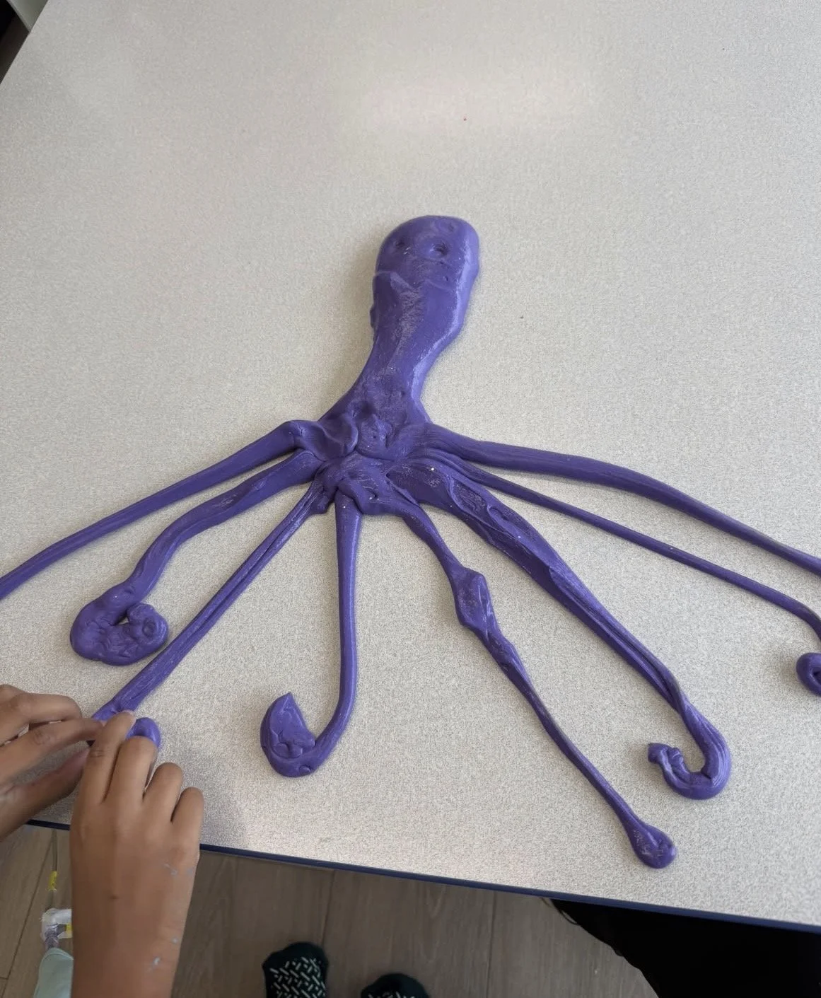 Kids crafting purple octopus sculpture on a tabletop.