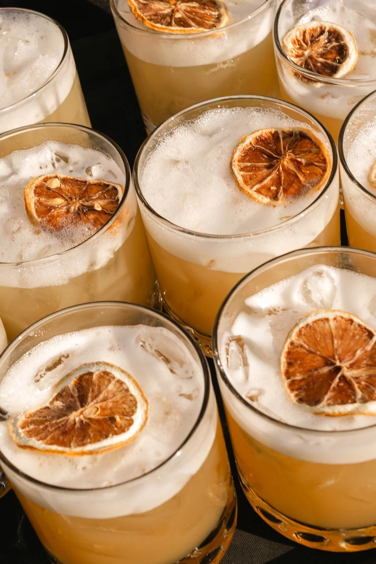Several glasses of a light-colored beverage with foam on top, garnished with dried citrus slices.