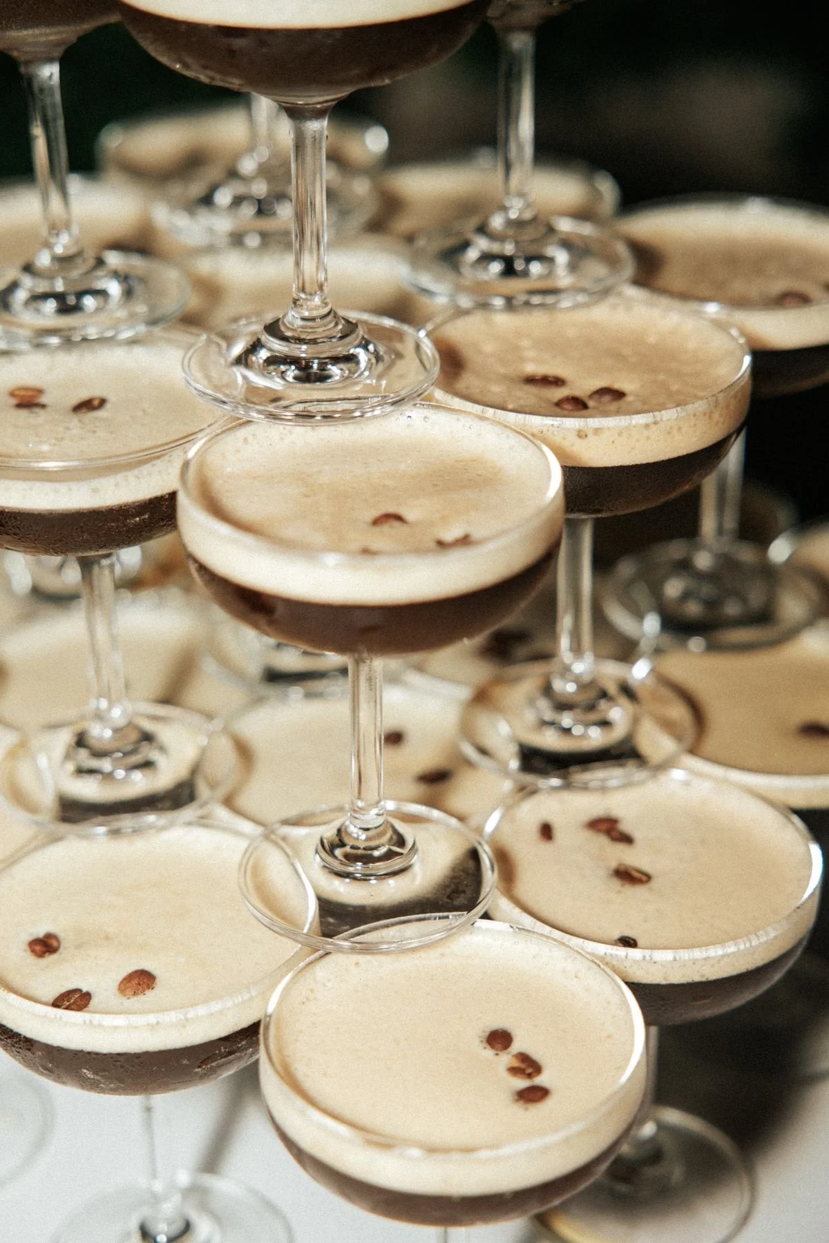 Multiple coupe glasses filled with layered espresso drinks topped with cream and garnished with coffee beans.