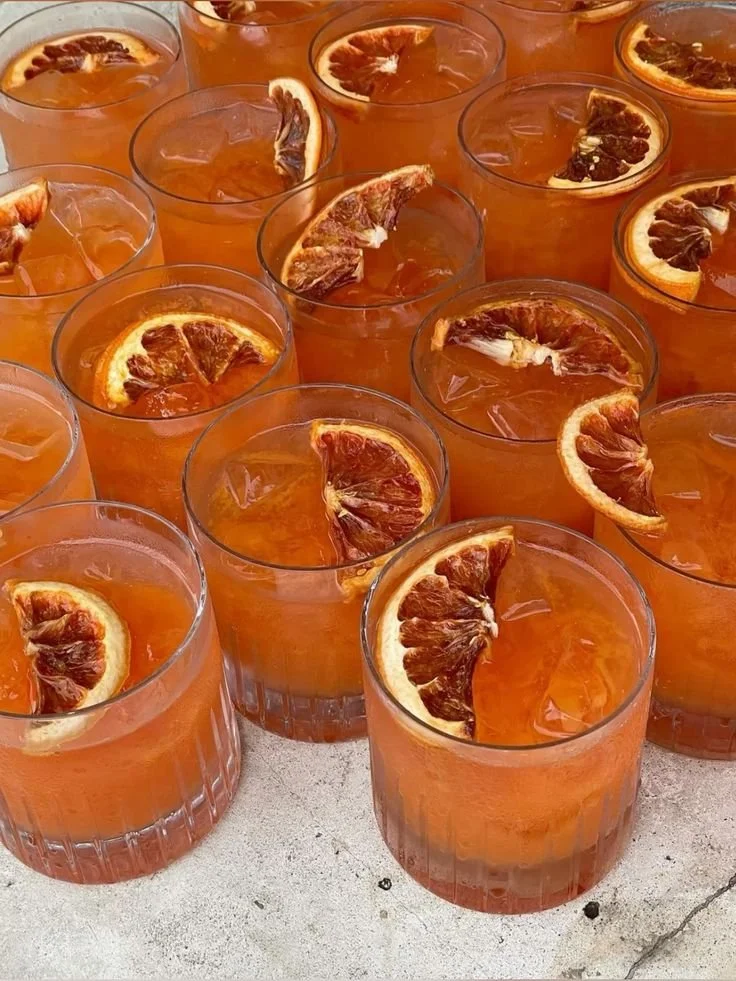 Multiple glasses of iced tea garnished with slices of blood orange on a light-colored surface.