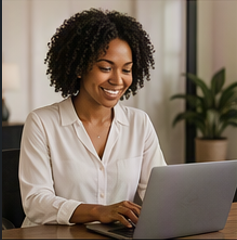 Woman with curly hair smiling while using a laptop in an office.