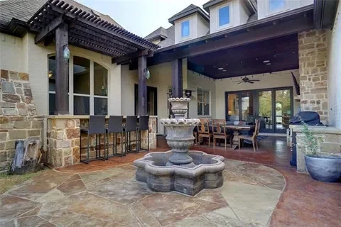Outdoor patio area with a stone fountain, wooden pergola, dining table, chairs, and potted plants