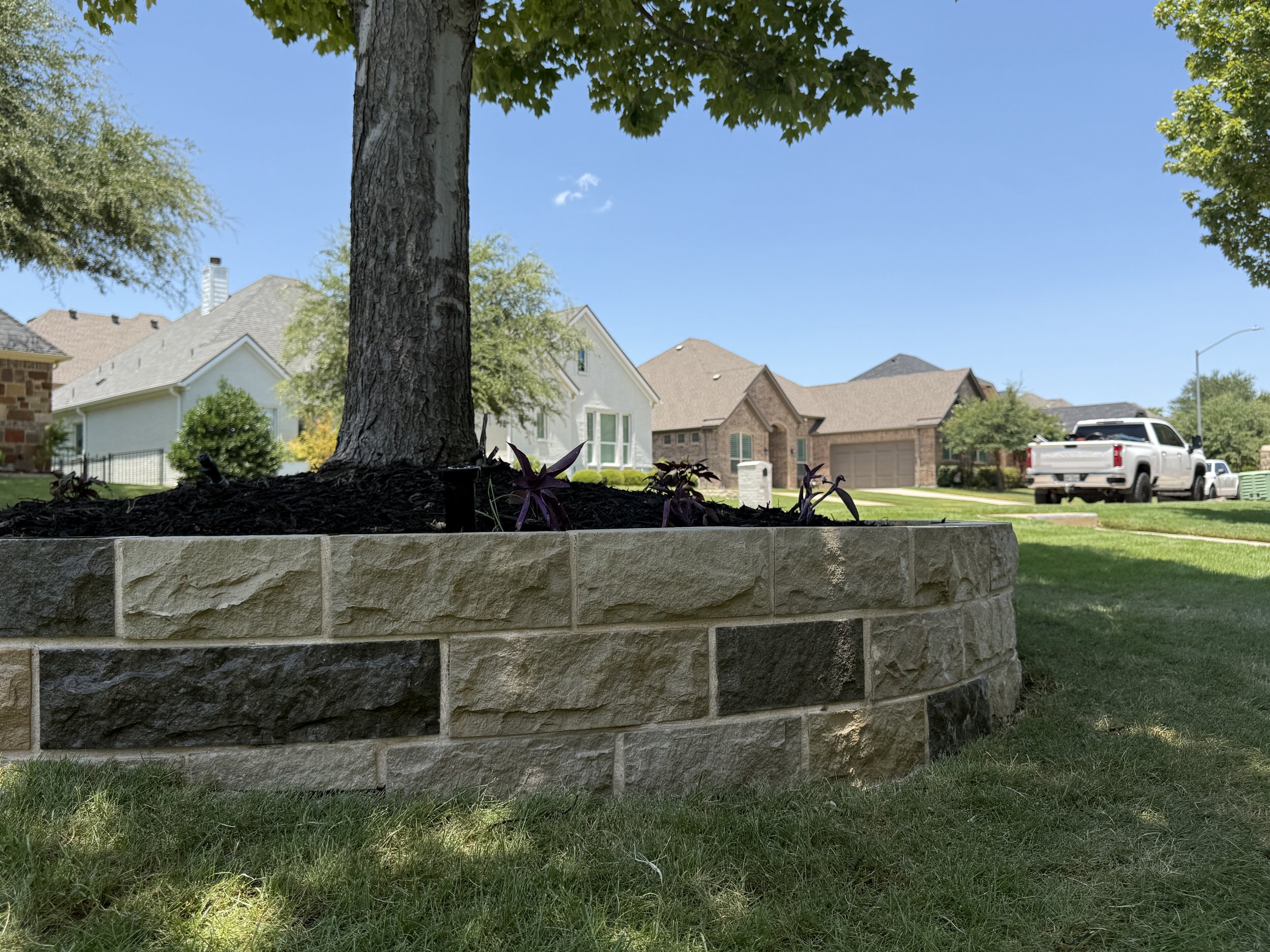 A residential neighborhood with houses, trees, and a white truck parked on the street under a clear blue sky.