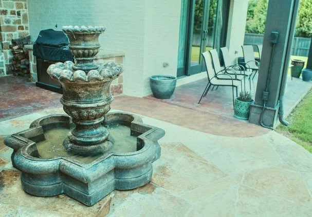 Outdoor patio with a decorative fountain, chairs, and potted plants next to a glass door.