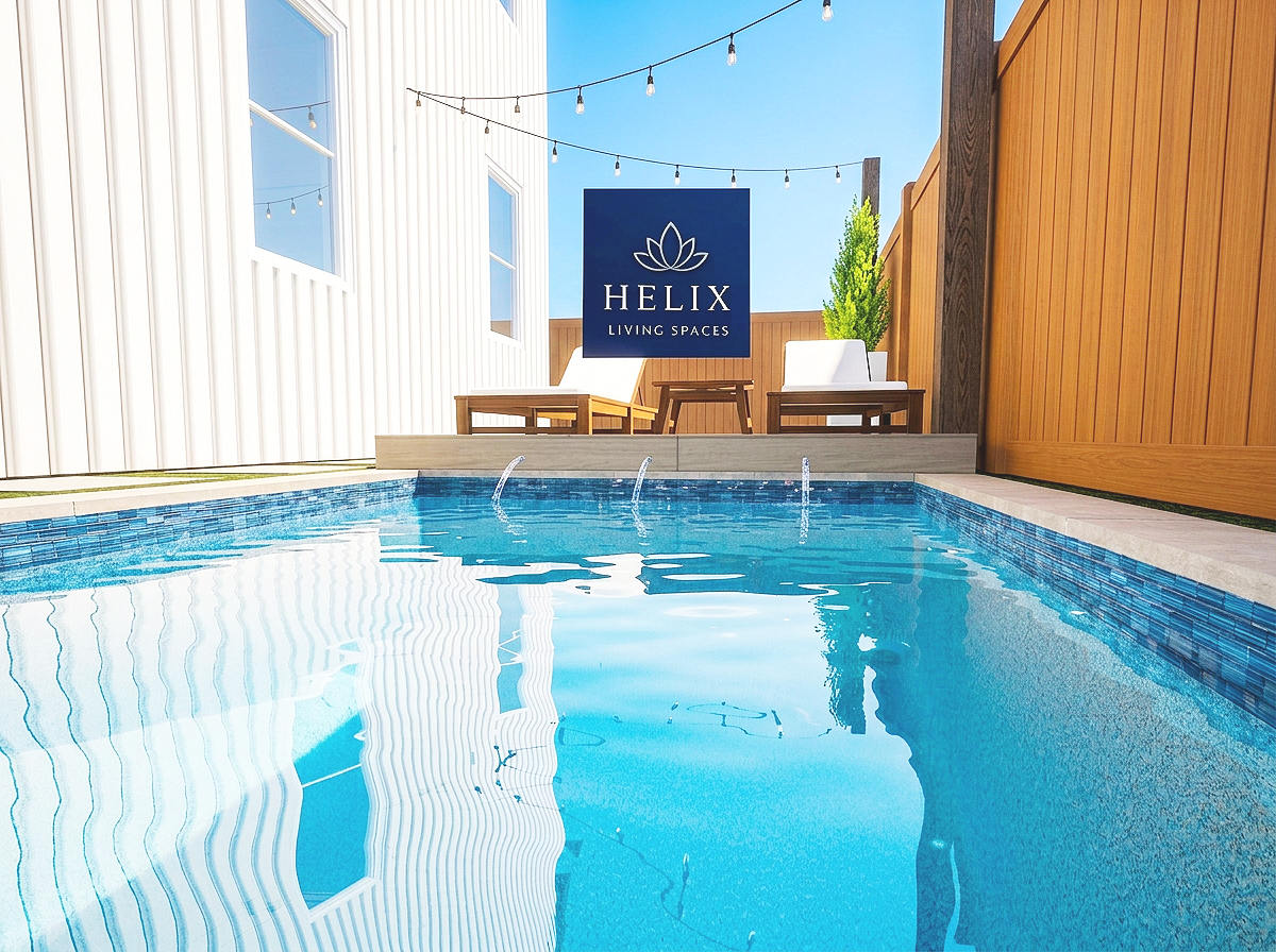 A small private pool with a blue tiled interior, surrounded by white and wooden fencing, with outdoor furniture and a sign that reads 'Helix Living Spaces' in the background, and string lights hanging above.