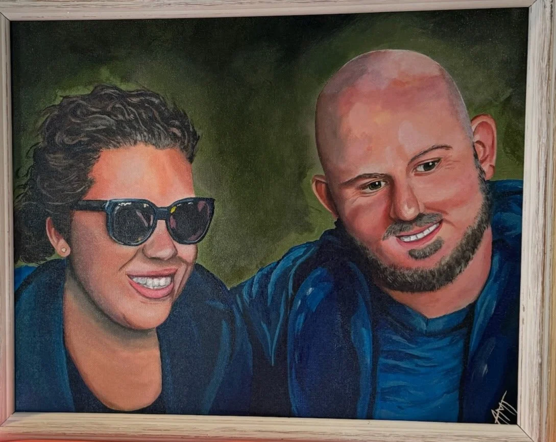 A painting of a woman with short dark hair wearing sunglasses and a man with a shaved head and beard, smiling. Both are wearing blue clothing.
