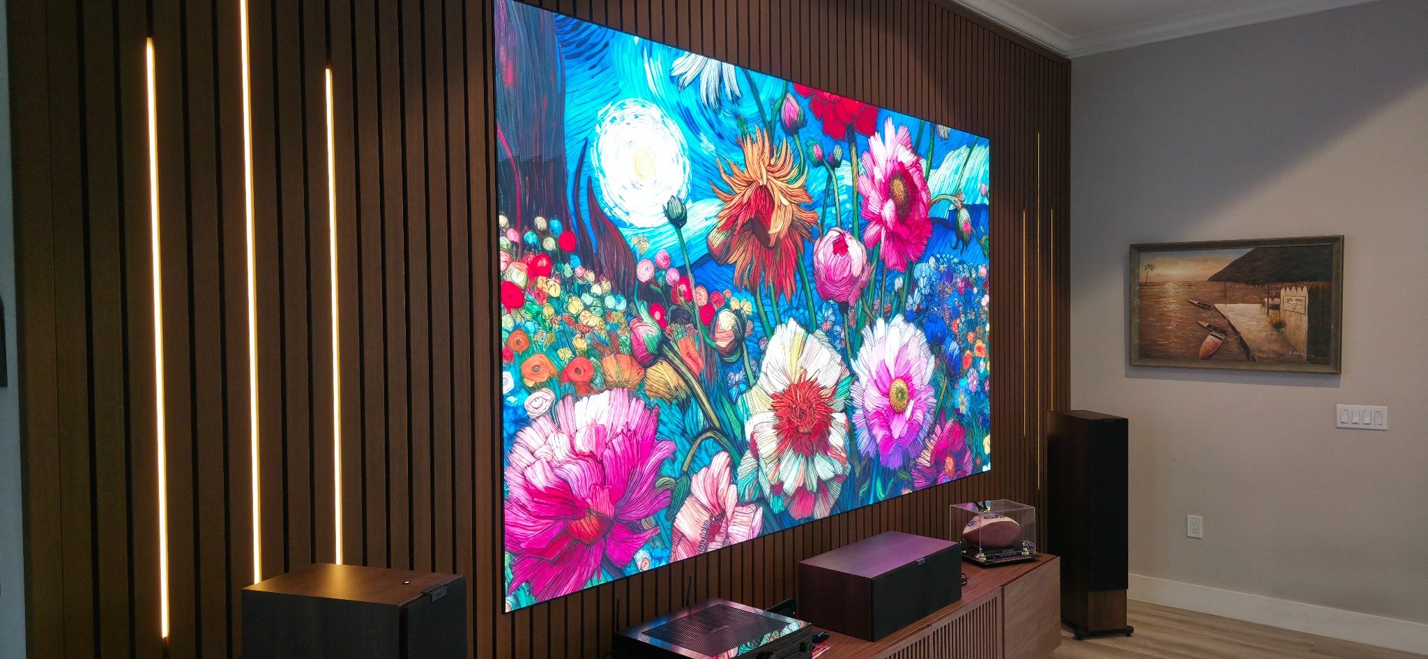 A large brightly lit digital artwork of colorful flowers and a moon on a wooden wall in a living room.