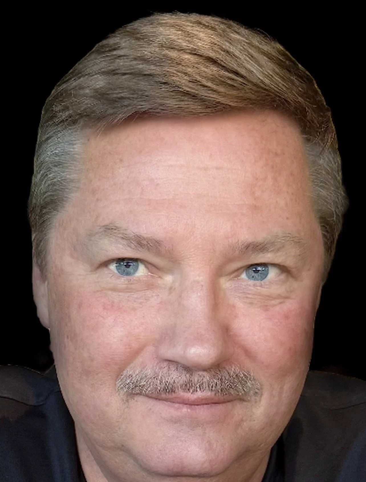Close-up of a middle-aged man's face with blue eyes, light skin, gray hair, and a trimmed mustache and beard. He is looking at the camera with a slight smile.
