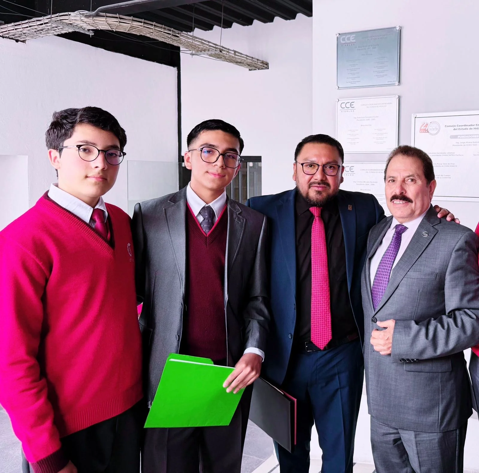 Cuatro hombres con gafas en un entorno formal posando para la foto, con certificados en la pared de fondo.