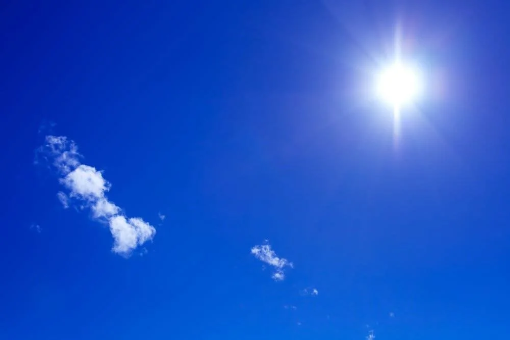 Clear blue sky with a bright sun and a few small white clouds.