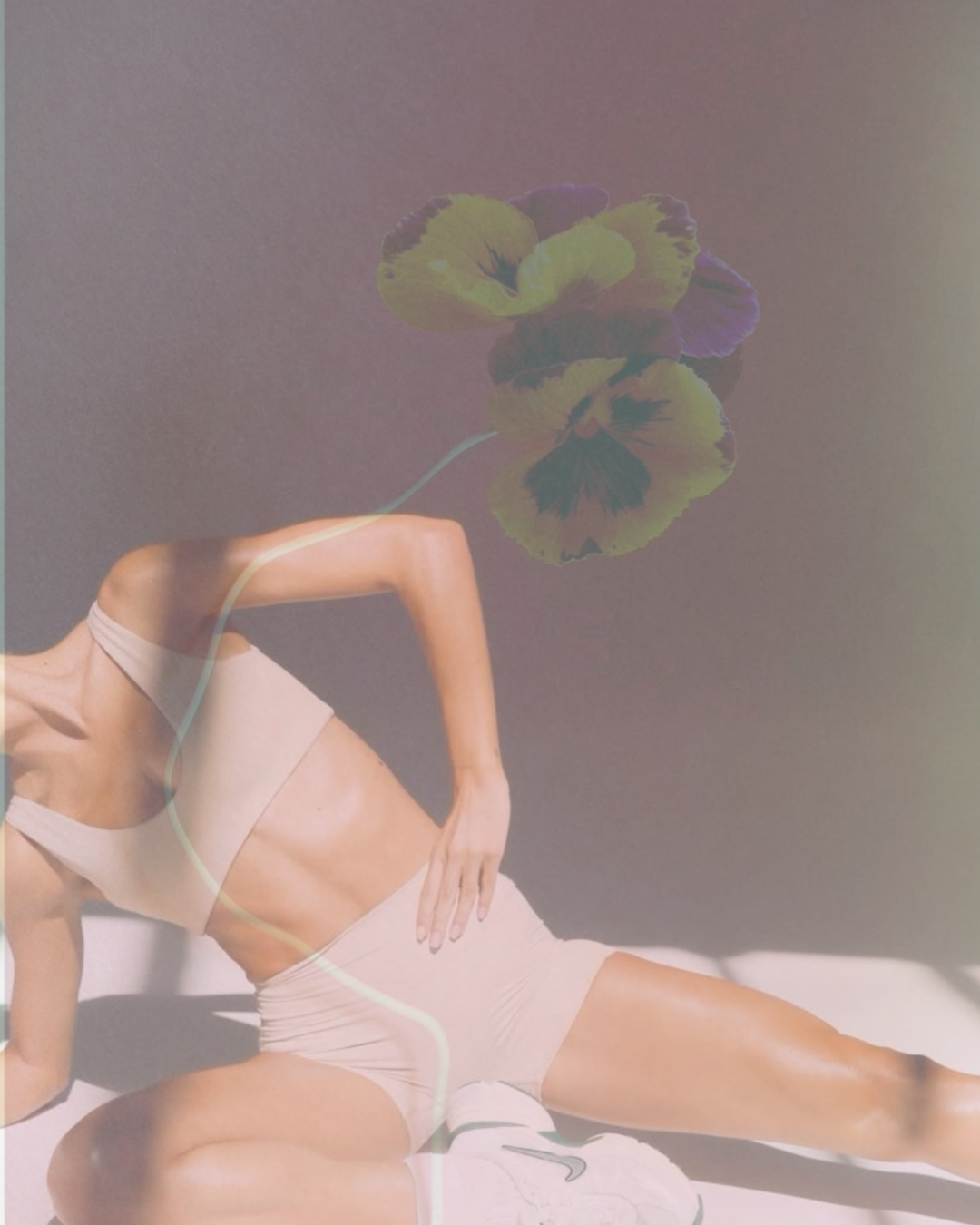 A woman in beige athletic wear posing on the floor with her hand on her hip, with a multicolored pansy flower and a faint green line overlayed in the image.