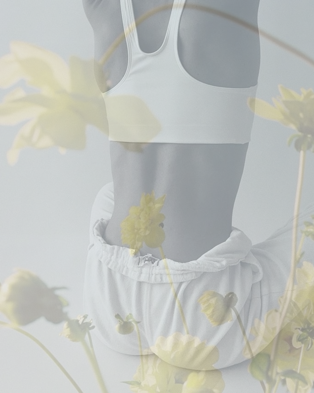 A woman wearing a white sports bra and white sweatpants, with her midriff exposed, is seen through a double exposure effect with yellow flowers.