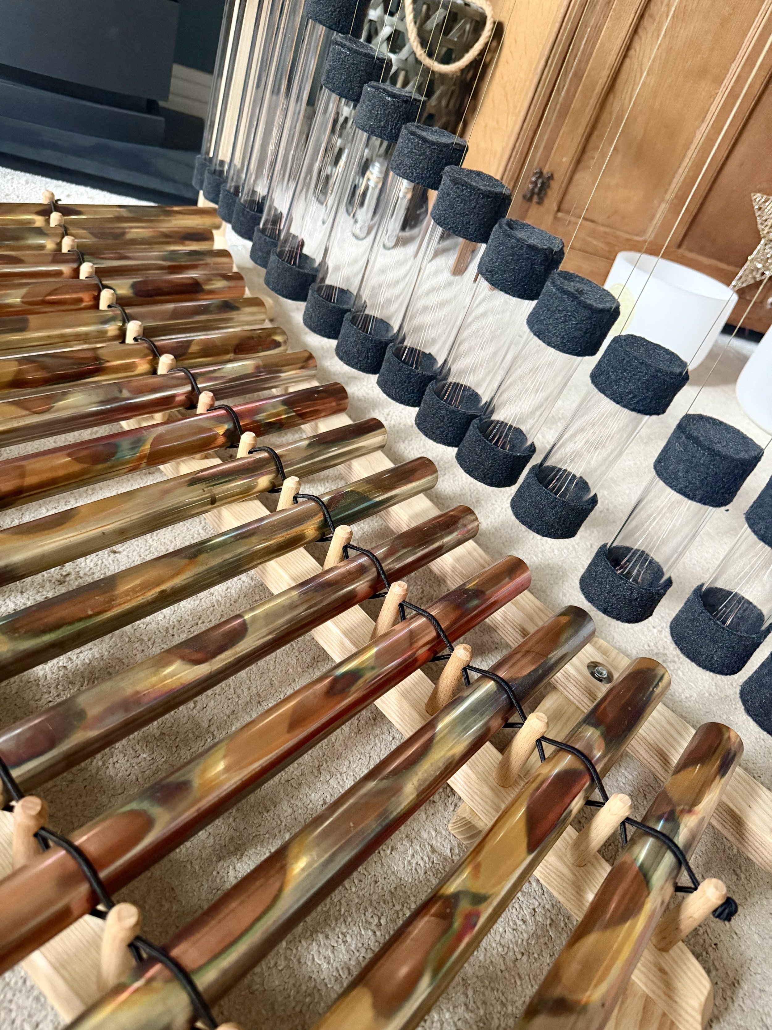 A collection of glass wind chimes with black foam covers hanging from thin, transparent strings, placed on a light-colored surface near wooden furniture.