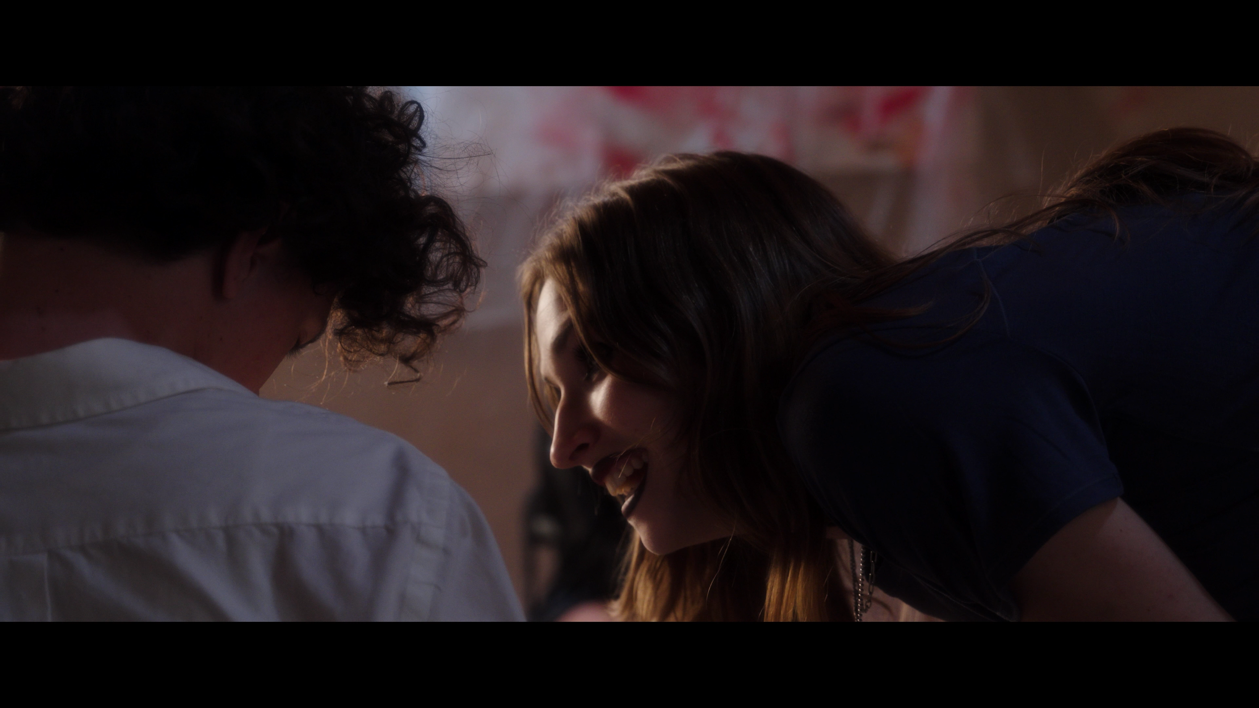 Two women and a man are closely together, smiling and laughing, with their heads bent towards each other, in a warm and joyful moment.