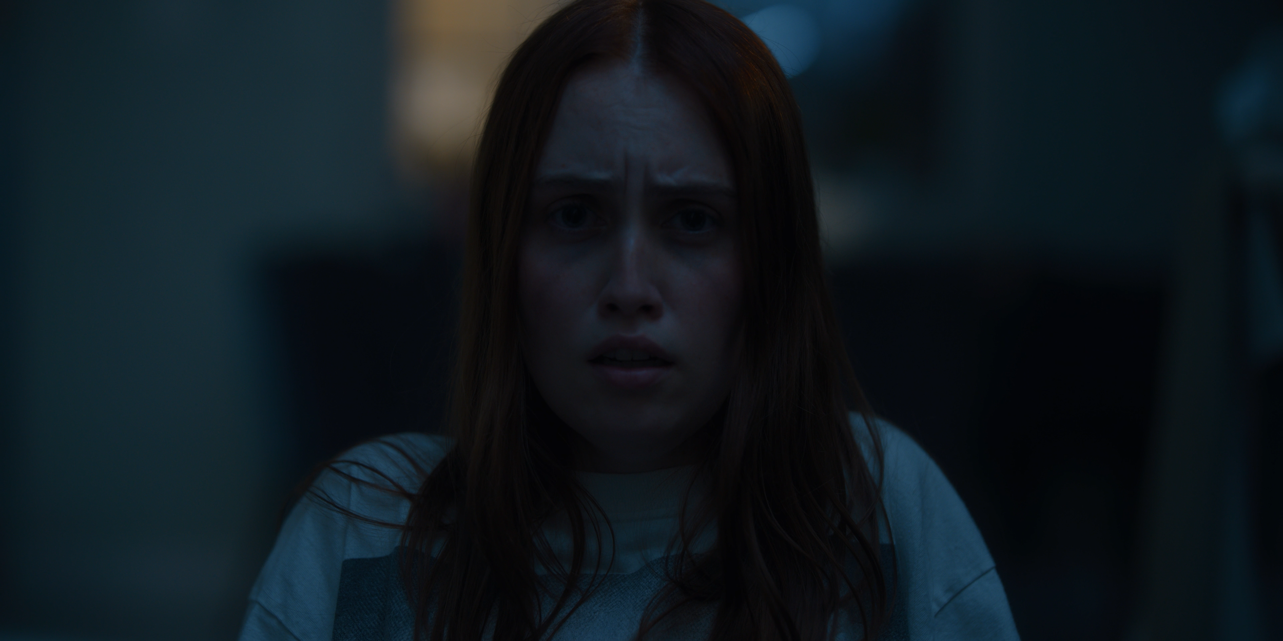 A young woman with red hair looking forward with a concerned expression on her face.