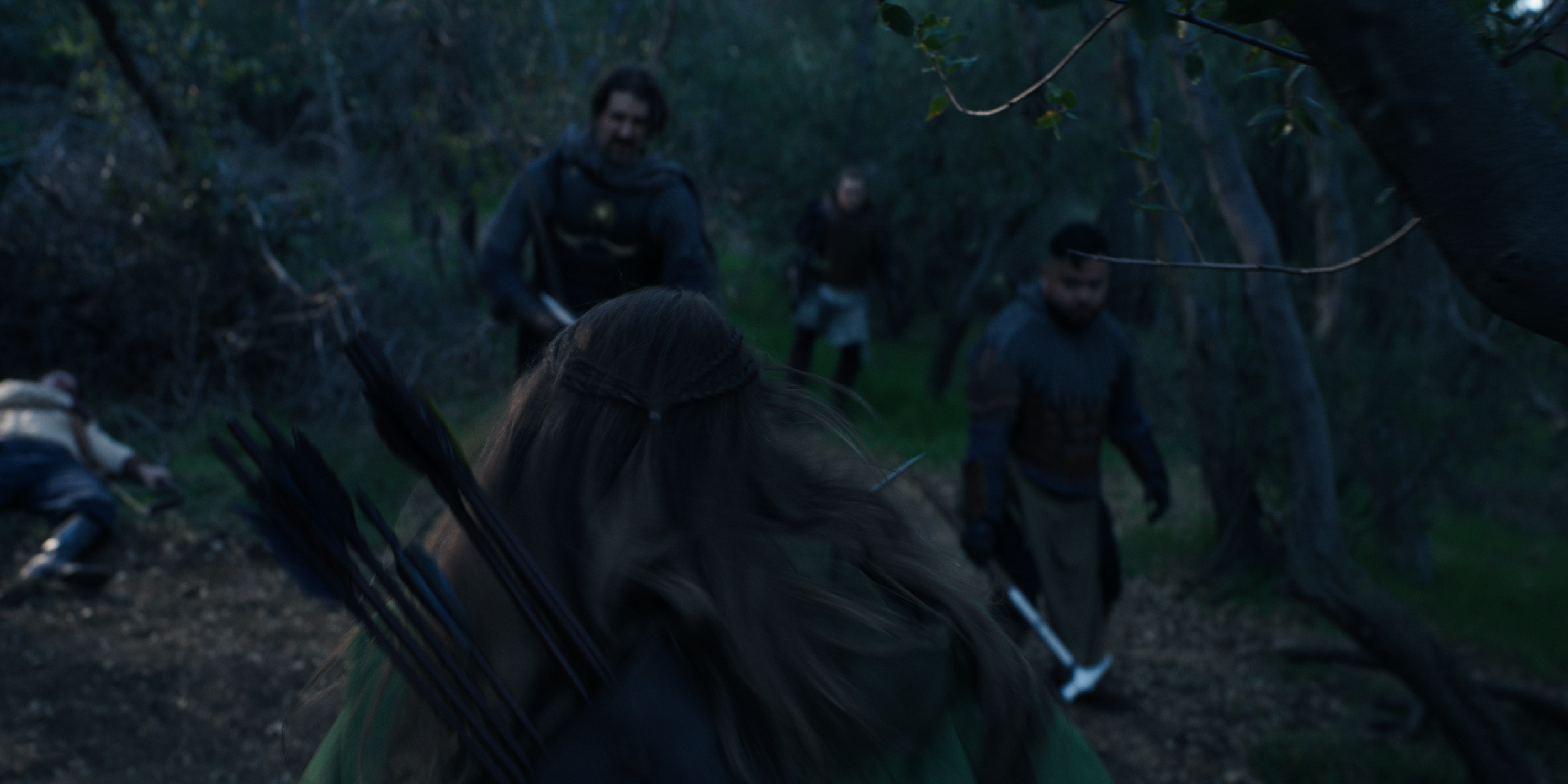 People in dark clothing and armor outdoors in a wooded area, some with bows, and a horse visible on the left.