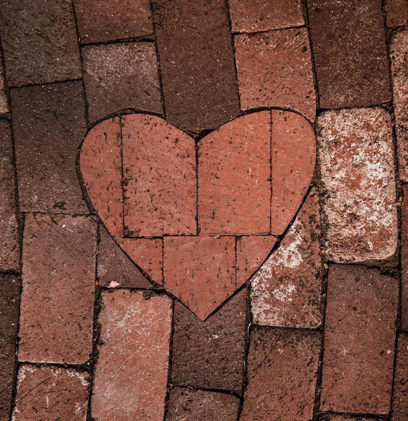 A heart shape is outlined on a brick sidewalk, created by arranging the bricks in the shape of a heart.