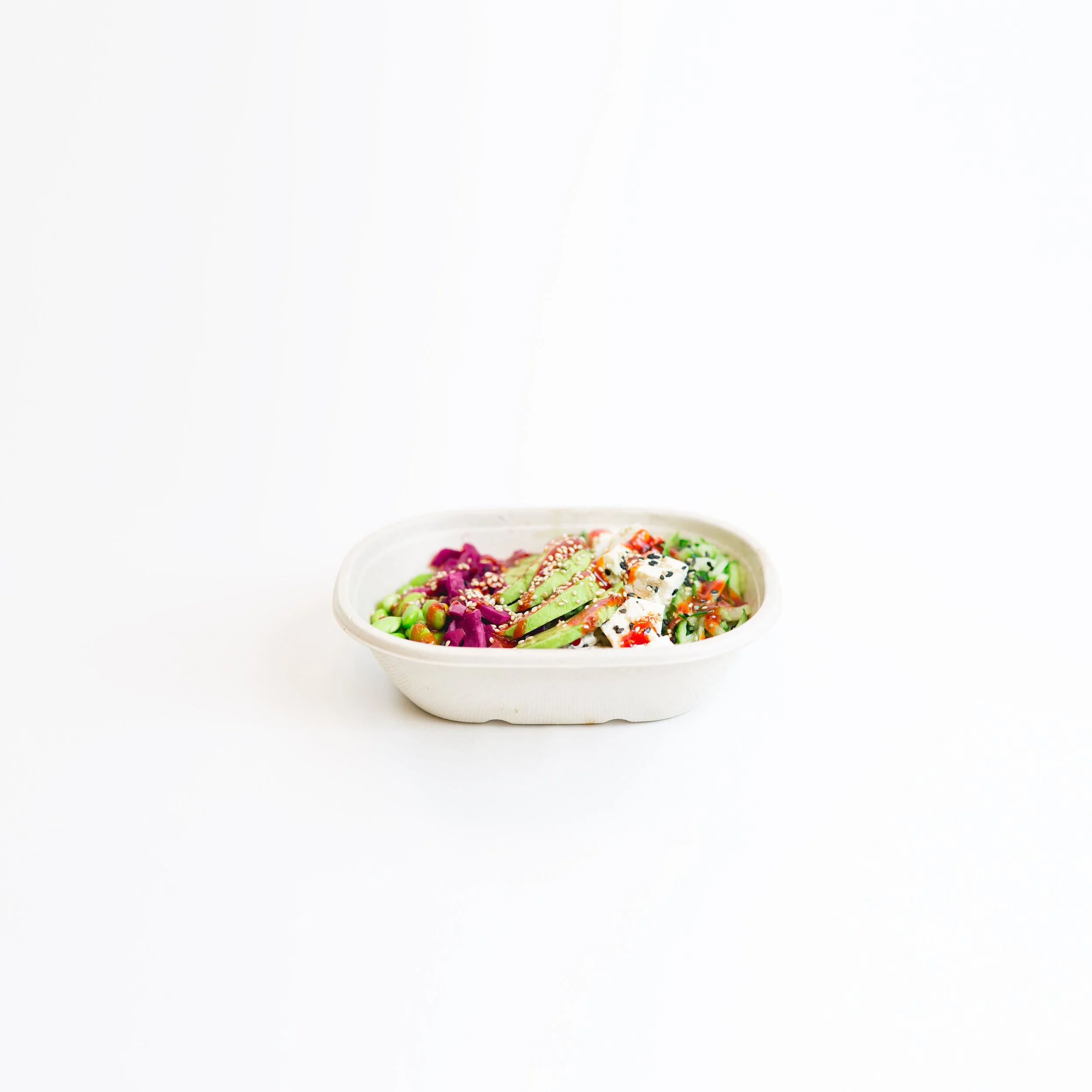 A white bowl filled with colorful, fresh vegetable salad topped with sesame seeds, served against a plain white background.