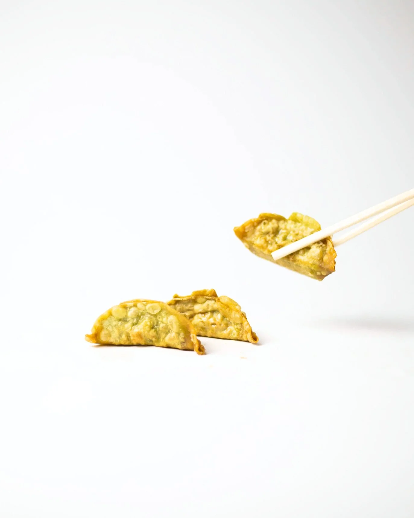 Close-up of two fried dumplings with one being held by chopsticks, all set against a plain white background.