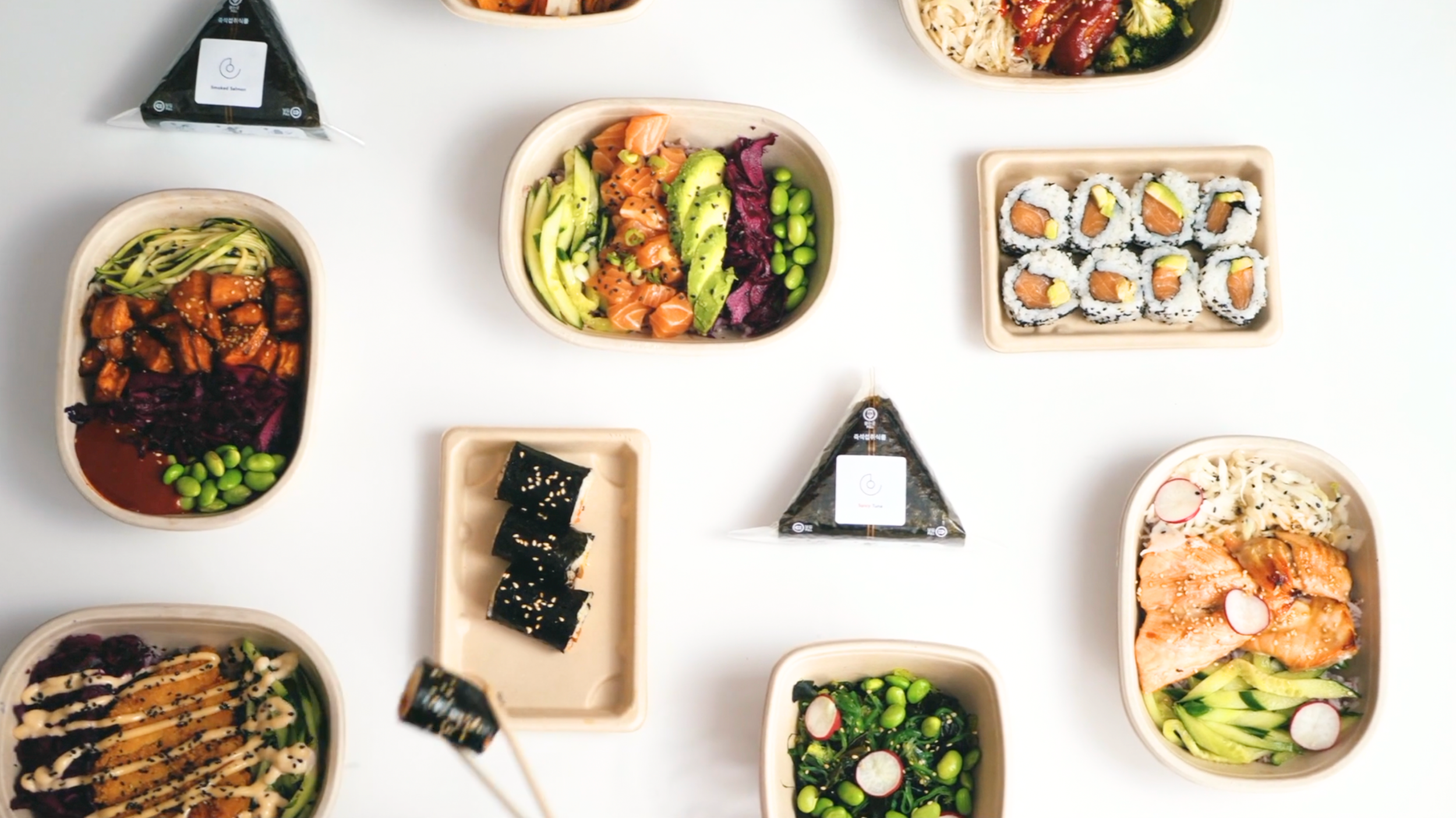 Assorted Japanese dishes including sushi rolls, bowls with rice, vegetables, grilled salmon, and seaweed wrap on a white table.