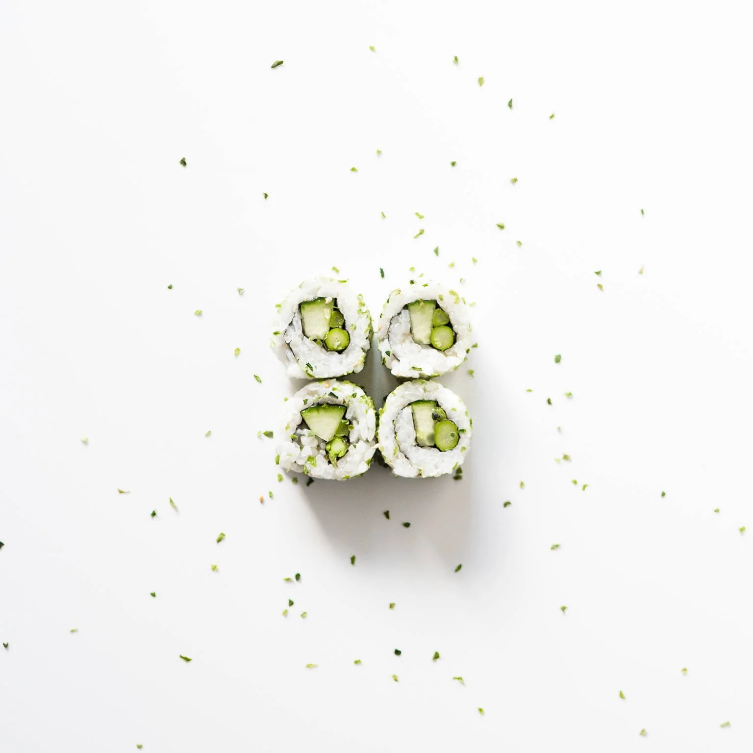 Four pieces of cucumber and rice sushi rolls with sesame seeds on a white background, sprinkled with chopped herbs.