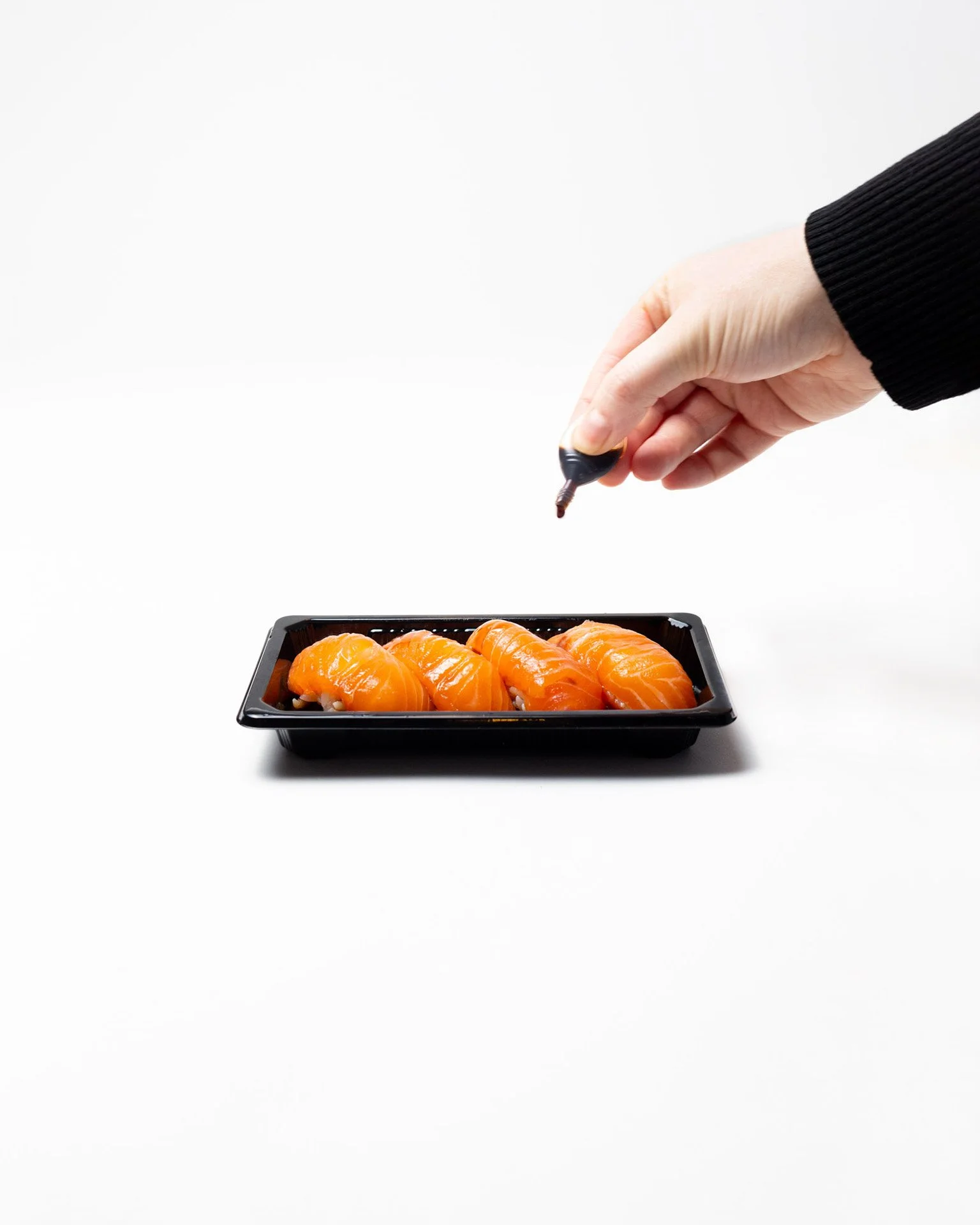 Hand holding a soy sauce bottle above a tray of salmon sushi.