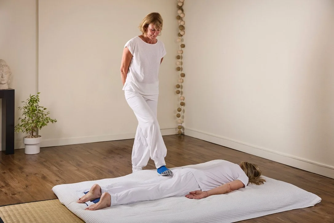 Une femme allongée sur un futon, reçoit un massage Sokuatsu, massage japonais avec les pieds.