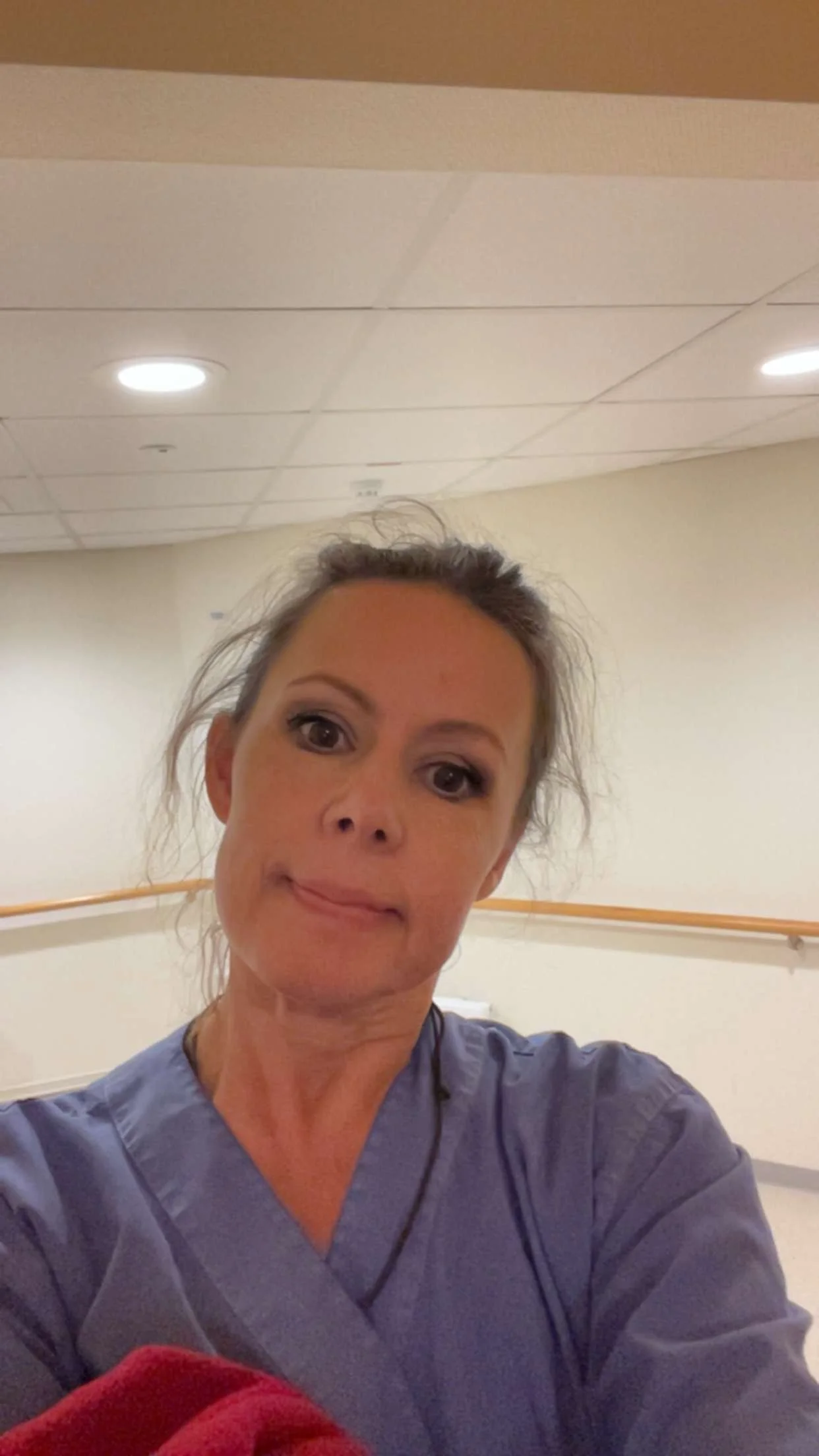 En kvinne tar et selfie i et rom med hvite vegger og taklys, hun har på seg sykepleieruniform.