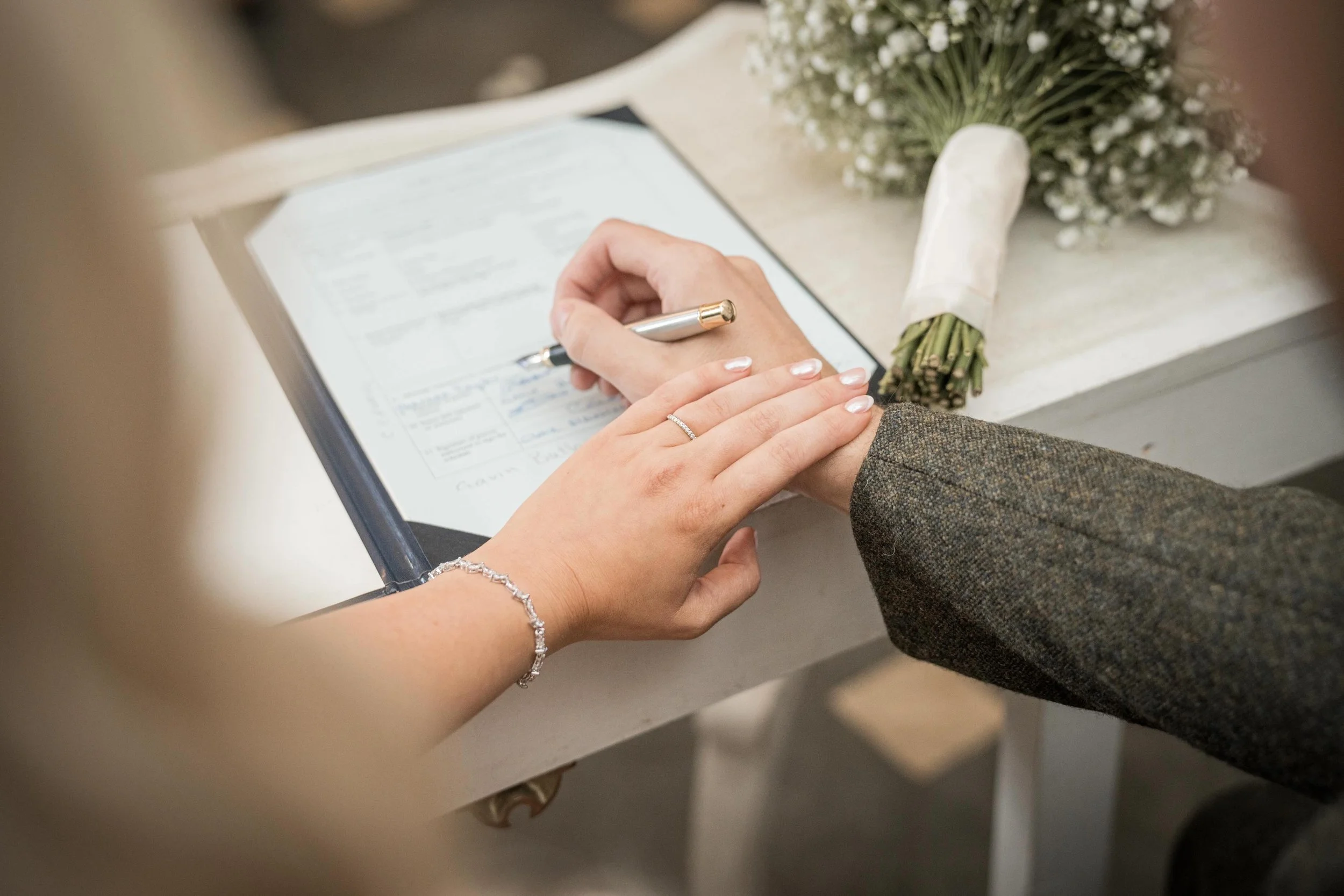 A bride and groom holding hands during a wedding ceremony, with a bouquet of white flowers on a table nearby.
