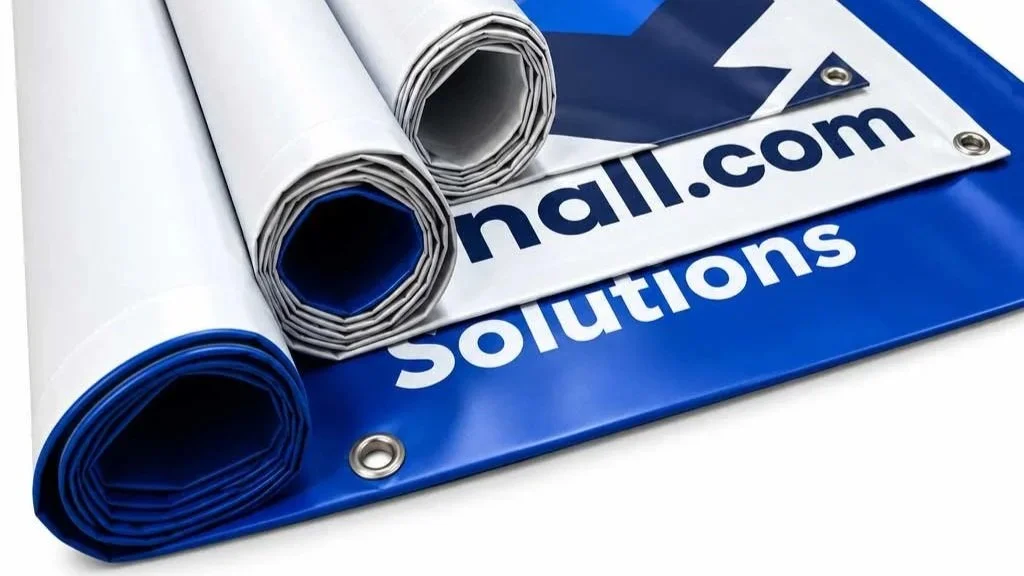 Rolls of banner and flag material with the text 'nail.com Solutions' on a blue background.