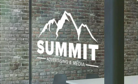 Logo of 'SUMMIT Advertising & Media' with mountain peaks design on a brick wall.