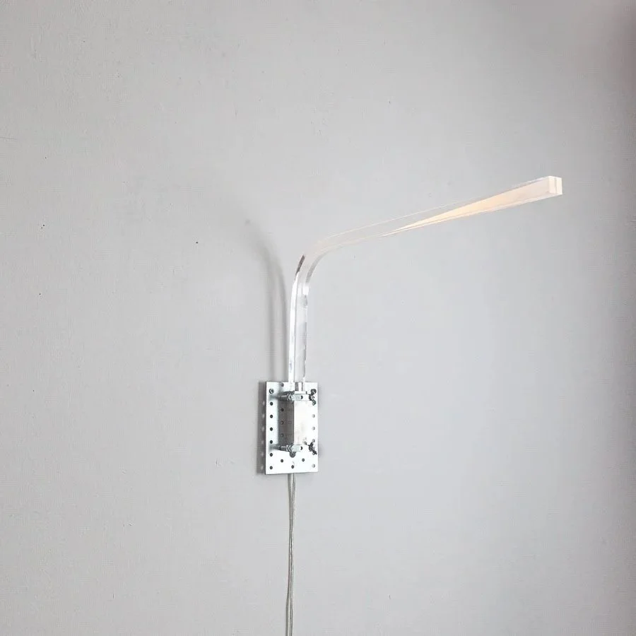 Ein wandmontiertes Gerät mit einem gebogenen, transparenten Arm, vermutlich eine LED-Leuchte, an einer weißen Wand.