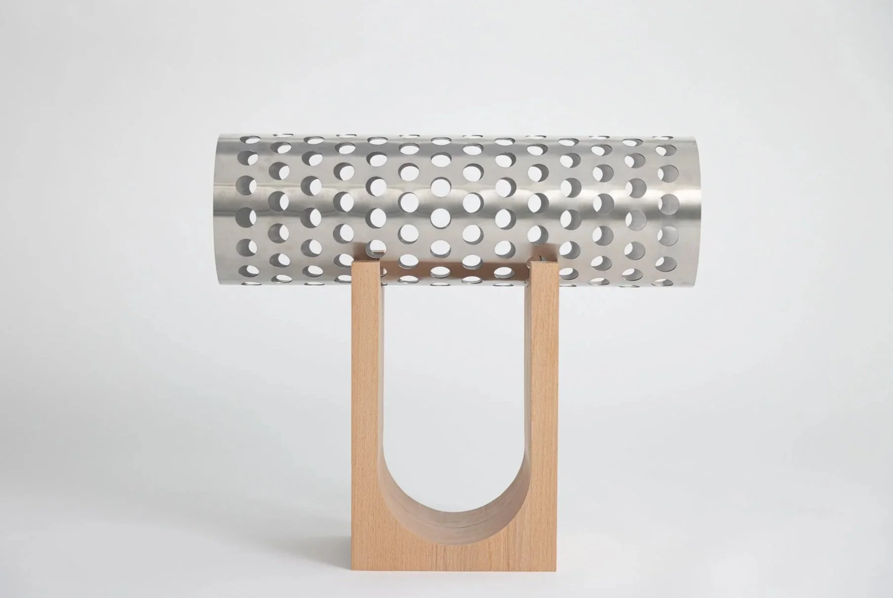 Ein modernes, minimalistisches Küchenutensil aus Metall mit Löchern, das auf einem Holzständer steht.