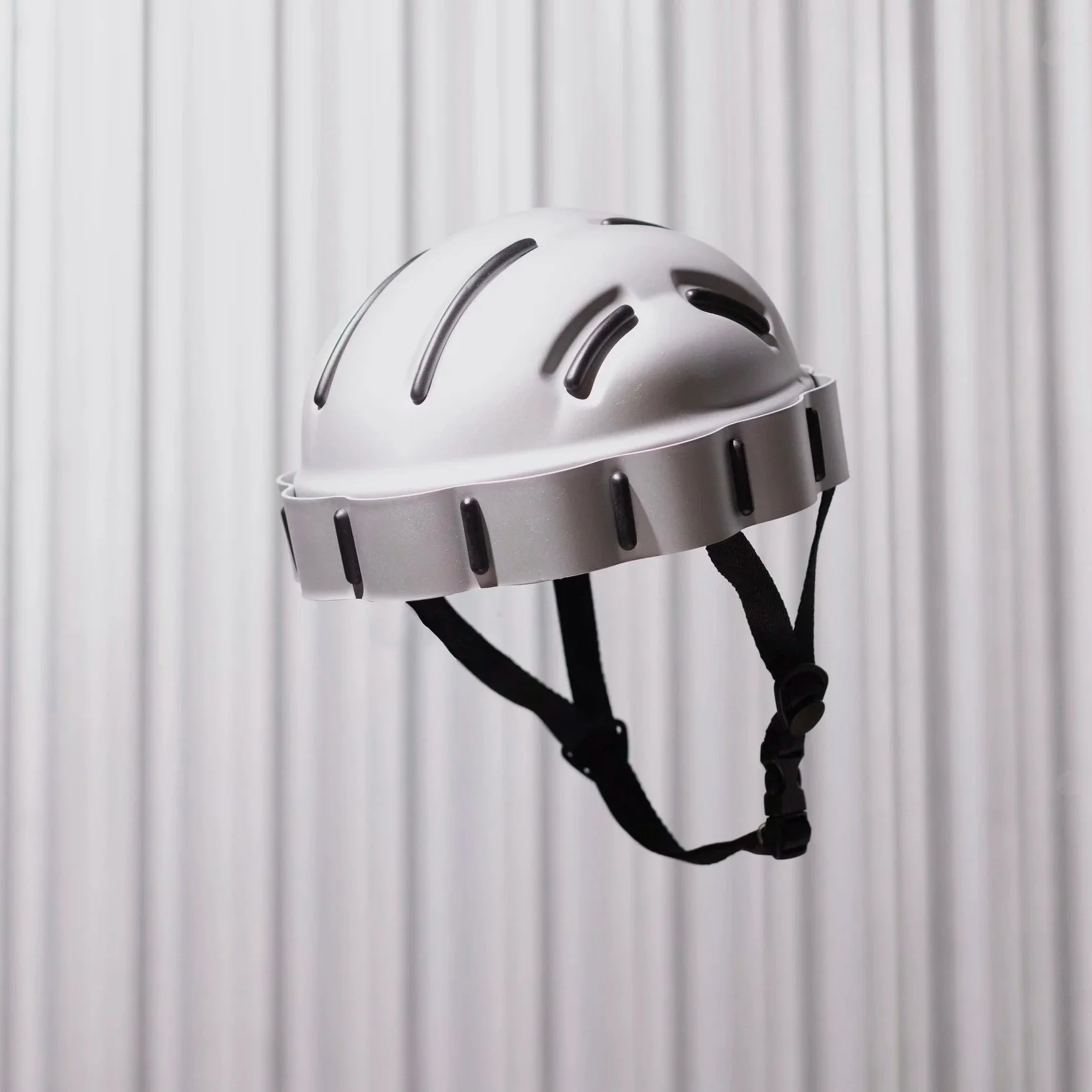 Aluminium Helmet flying in the air in front of silver packground with stripes. 