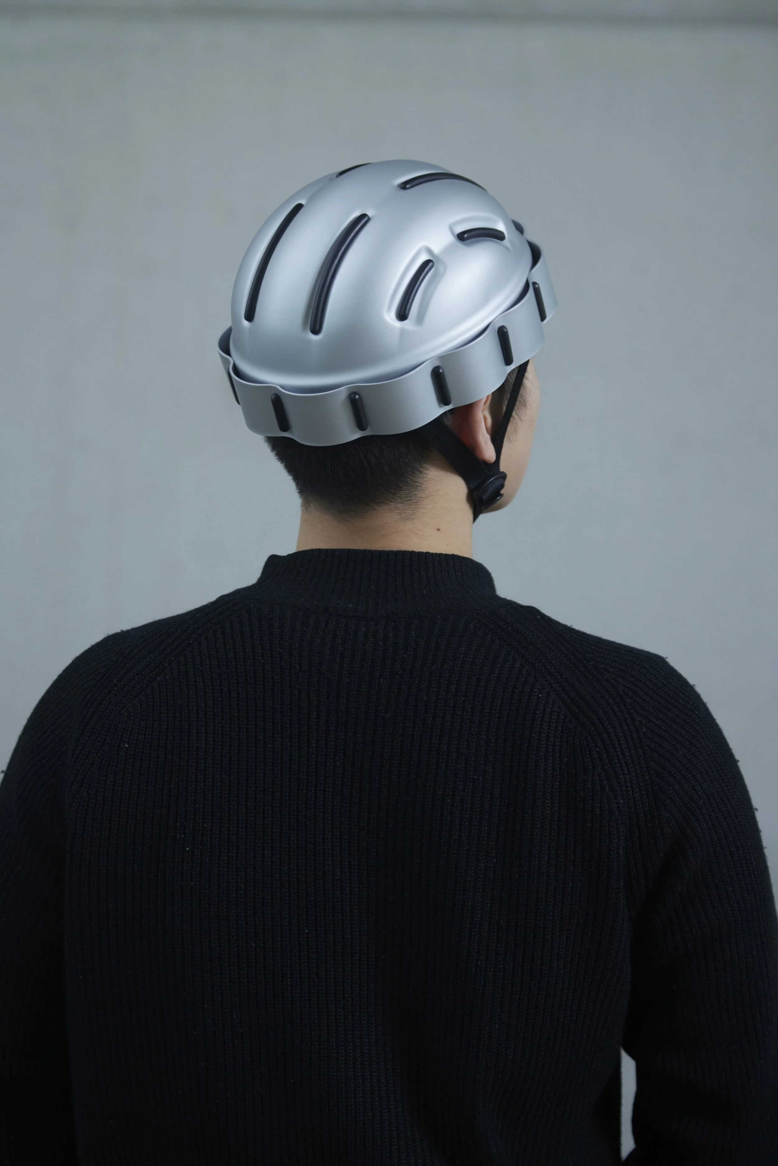Ein Mann trägt einen silbernen Fahrradhelm, gesehen von hinten gegen einen grauen Hintergrund.