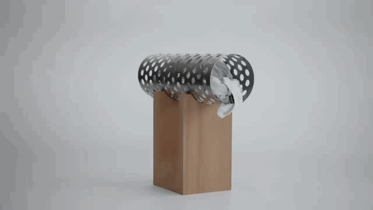 Empty trash can on wooden block with crumpled tissue and other trash inside, against a plain light gray background.