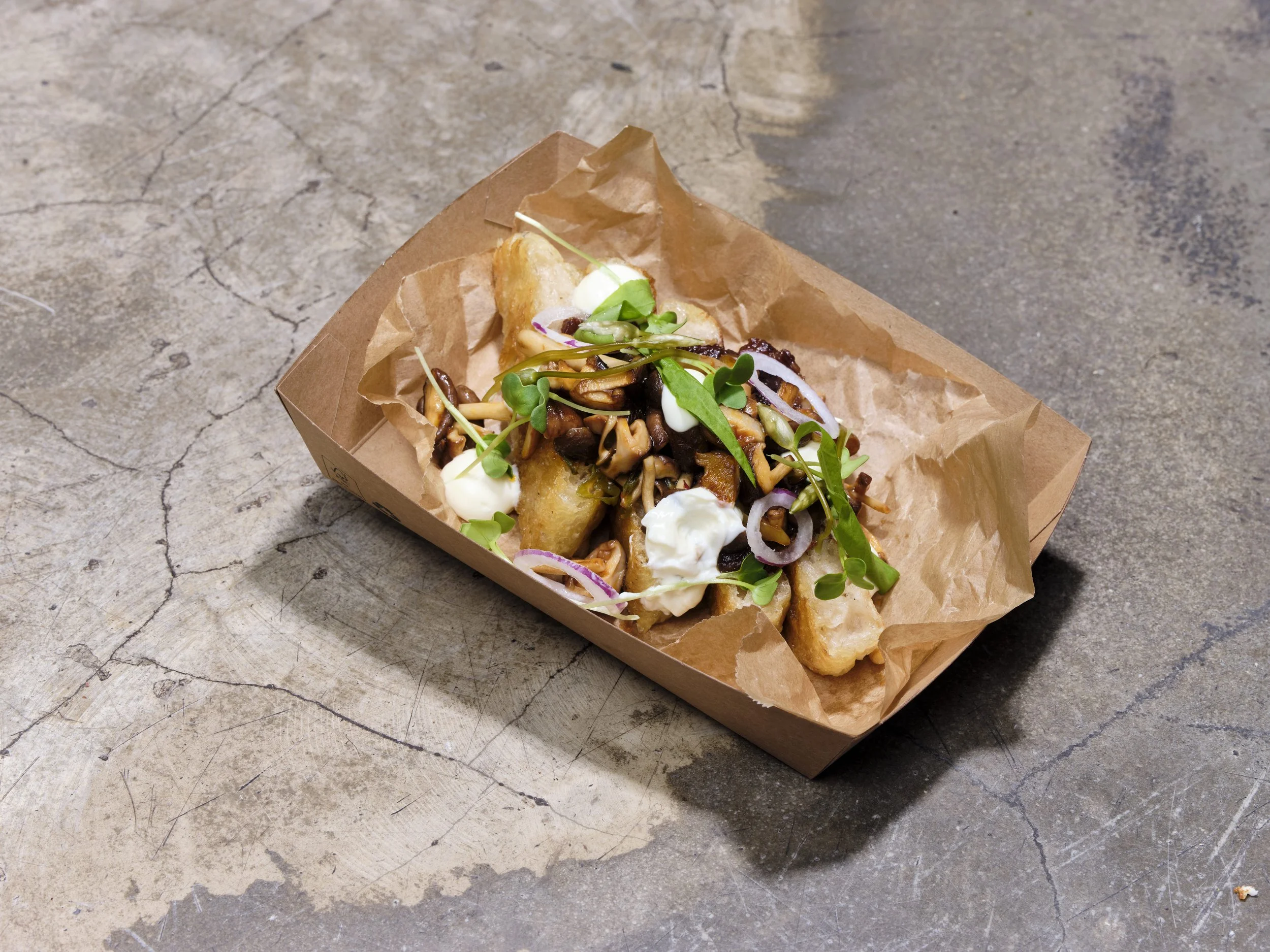 Ein pasando Pappschachtel mit einem Sandwich, das mit Salat, Zwiebeln, Soße und frittiertem Fisch gefüllt ist, liegt auf einer rauen, grauen Betonoberfläche.
