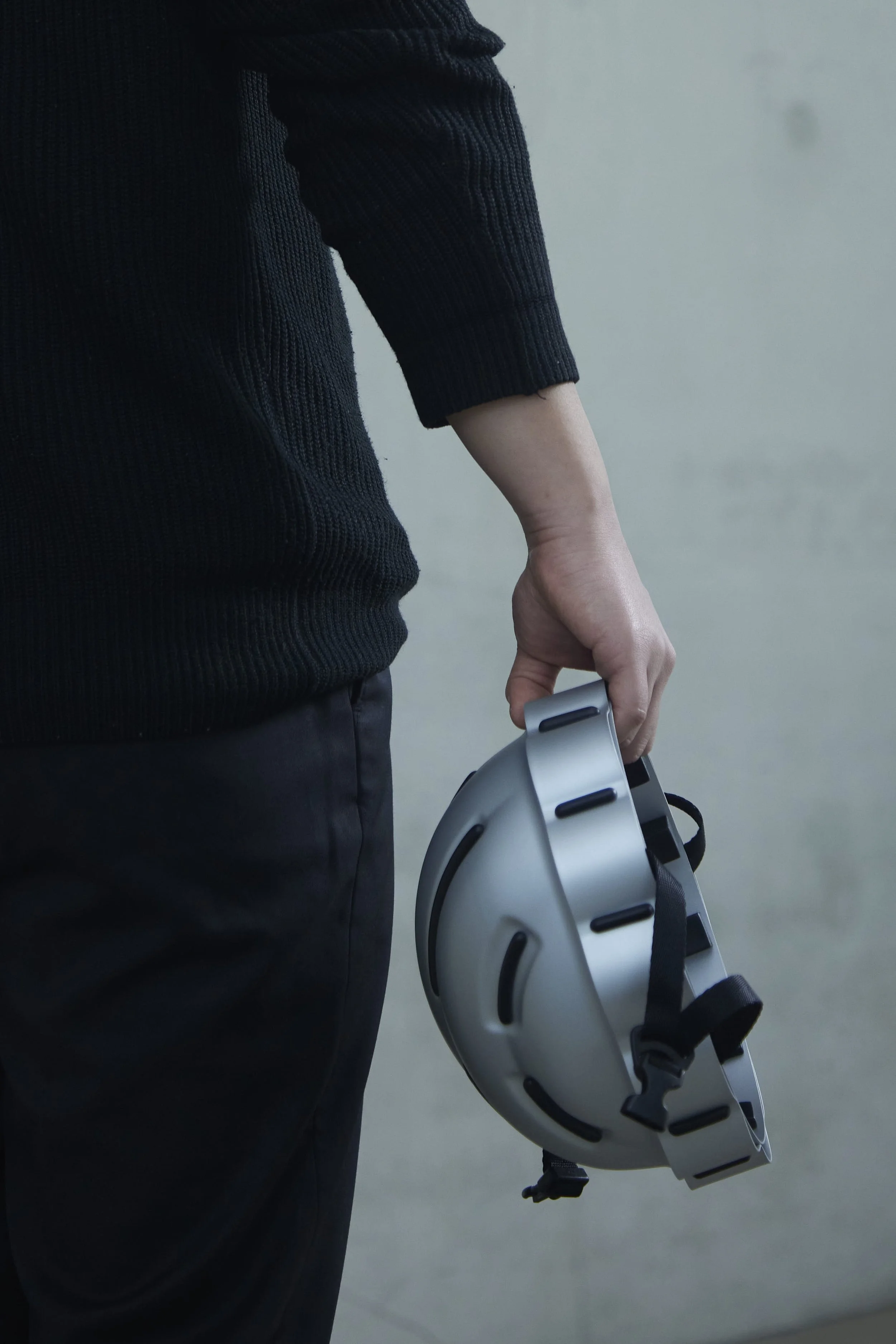 Person in dunkler, gerippter Pullover hält einen weißen Virtual-Reality-Helm in der Hand.